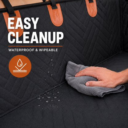 Black dog car seat cover with brown leather-like accents, shown with a hand wiping water off the surface to demonstrate its waterproof and wipeable cleanup feature. White and orange text overlays read 'EASY CLEANUP' and 'WATERPROOF & WIPEABLE'.