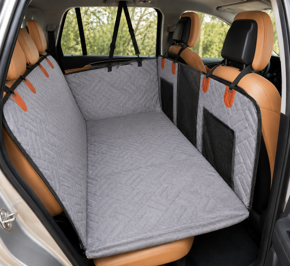 A gray dog car seat cover with black mesh side panels and orange pull tabs, shown installed in the rear cargo area of a vehicle with tan leather seats.